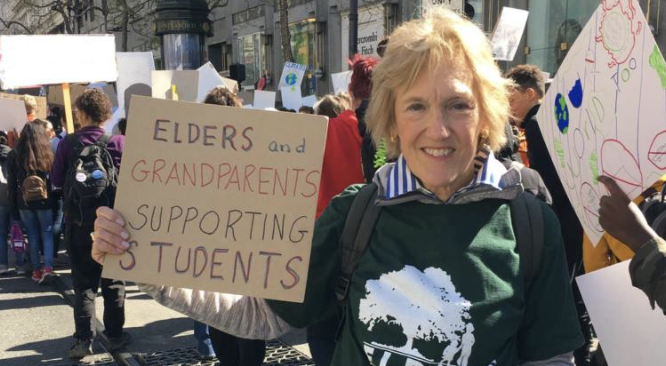 An older caucasian woman holds up a protest sign that says "elders and grandparents supporting students"