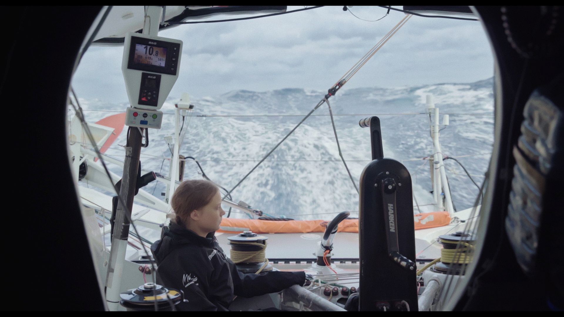Greta Thunberg sits on a boat in the foreground with the ocean in the background